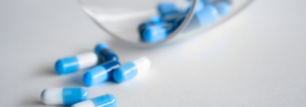 Blue and white medication capsules spilled onto a surface, representing clinical prescribing and pharmacy practice.