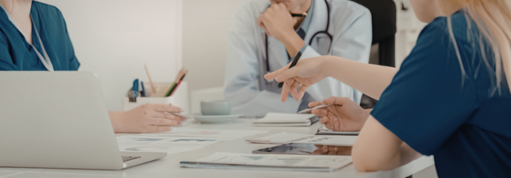 Healthcare professionals in a meeting reviewing documents and discussing workforce planning at a desk with a laptop and notes.
